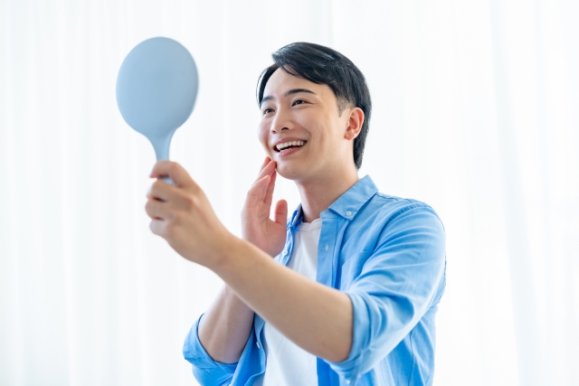 鏡で顔を見て肌が潤っている男性のイメージ画像